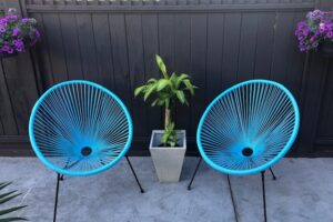 2 blue colored Acapulco chairs with a plant between them.