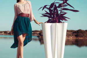 A woman in a green skirt stands next to a Vondom bye bye planter in white with lake in background.