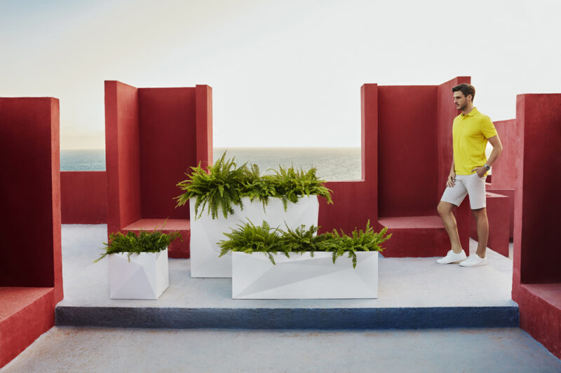 Different sized faz wall planter by Vondom in white with green planters and red patio chairs in background.