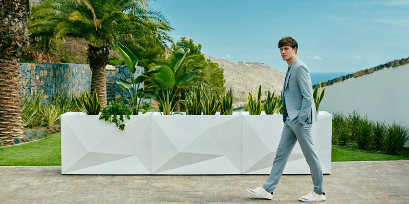 A man walks past 3 white Faz wall planters by Vondom with green plants in them.